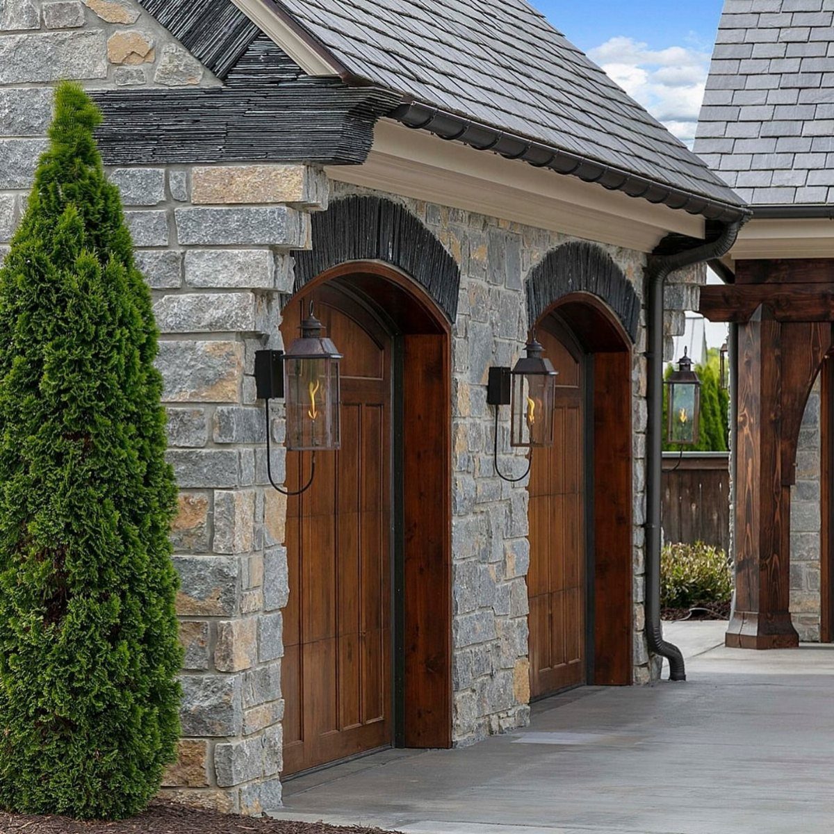 Black lantern outdoor lighting fixtures mounted on stone walls next to arched wooden doors.