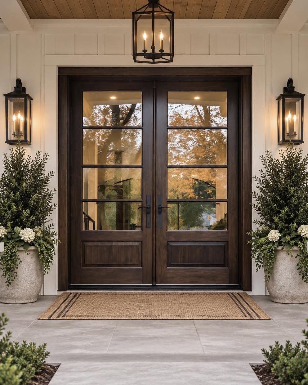 Dark wood double doors with glass panes flanked by black lanterns and potted greenery.