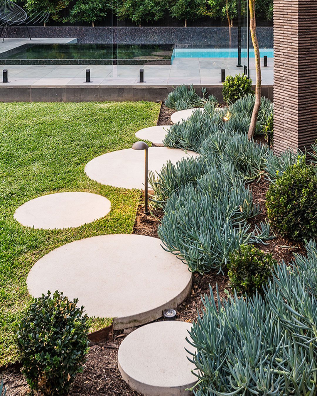 Circular concrete stepping stones forming a curved path through green grass and succulent garden beds.