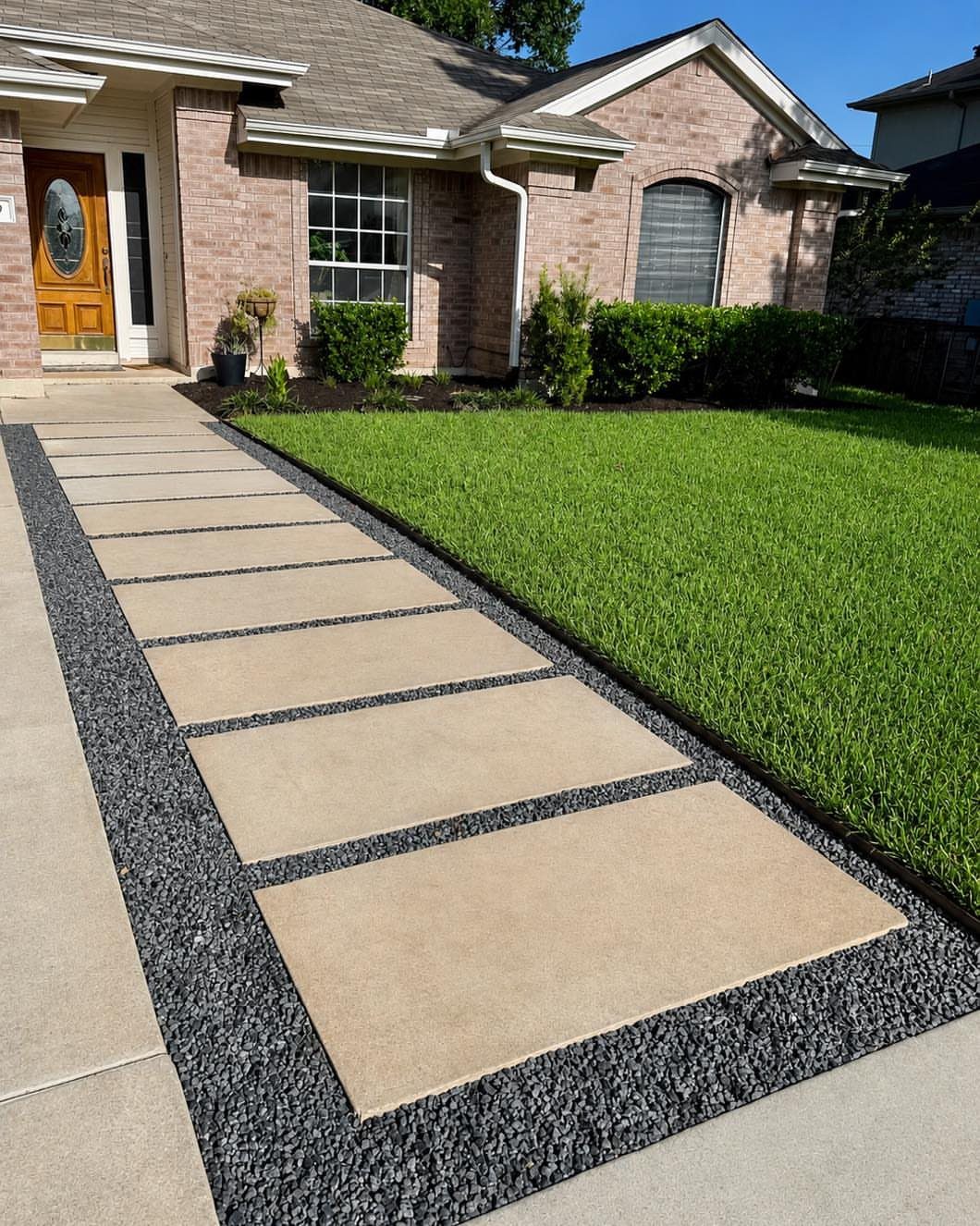 Large rectangular tan pavers set in dark grey gravel forming a linear walkway next to a lawn.