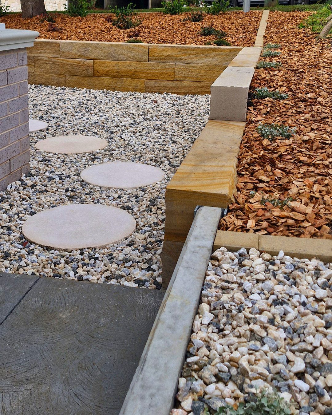 Circular stepping stones set in a bed of grey pebbles next to a sandstone wall.