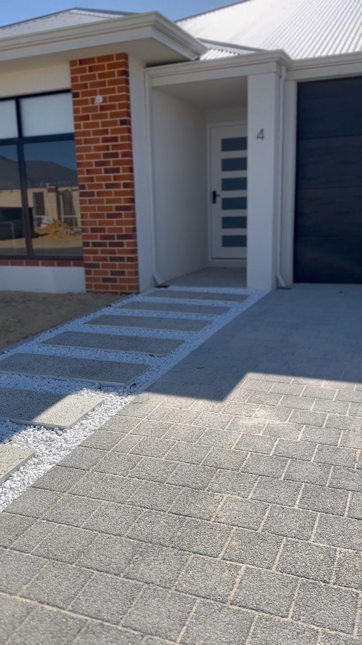 Rectangular grey stepping stones set into white decorative gravel leading to a modern house entrance.