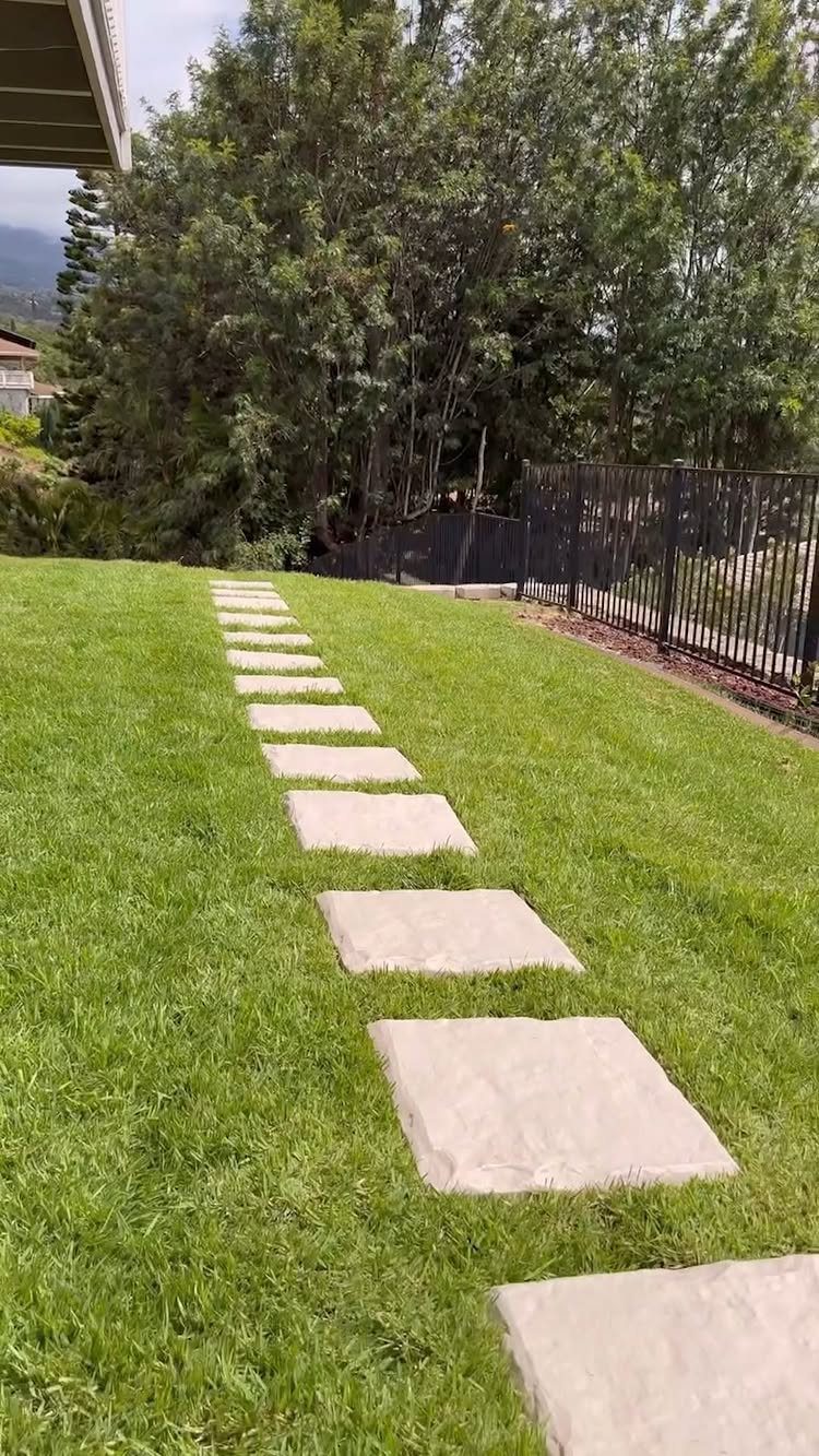 Large rectangular stone pavers forming a path through a green grass lawn towards trees.