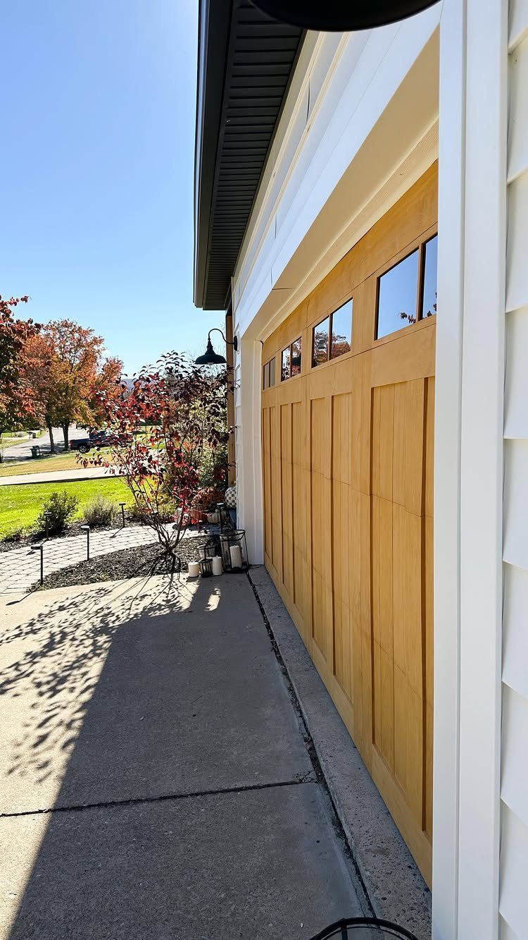 9 Garage Door Makeover Ideas for Instant Curb Appeal 5 A light wood-textured garage door with small windows installed on a white house exterior.