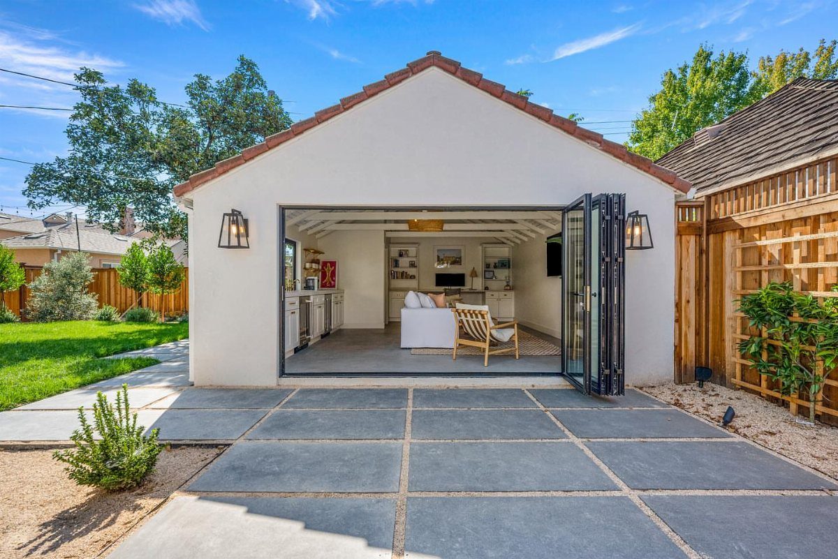 Turning a Garage to a Studio Apartment: 9 Layouts That Work 1 Modern studio apartment with open folding glass doors revealing a bright living area and kitchenette.