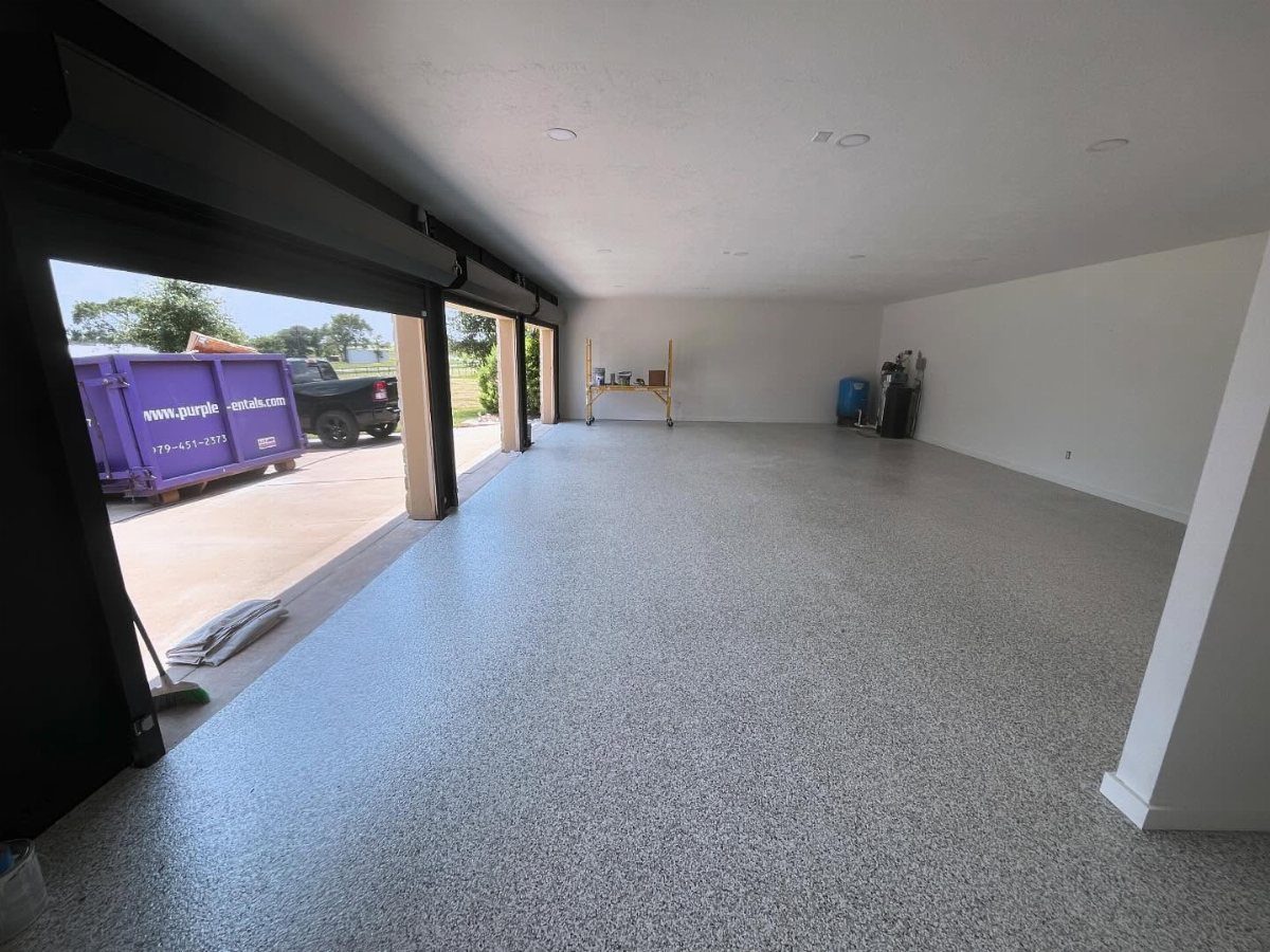 9 Garage Paint Colors for Doors, Floors, Walls and Ceiling 5 A spacious empty garage featuring light grey speckled epoxy flooring and white walls with an open door.