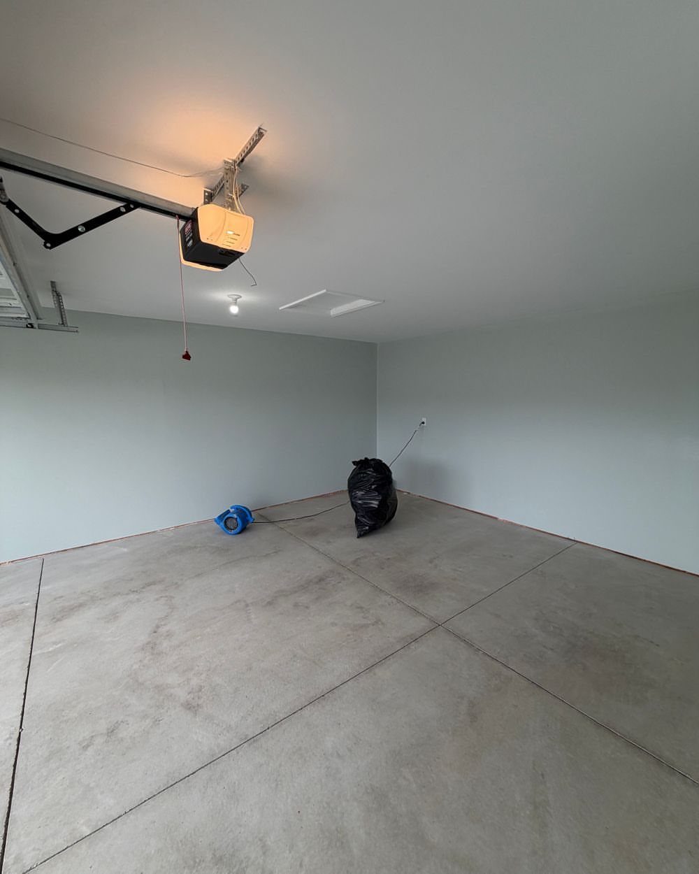9 Garage Paint Colors for Doors, Floors, Walls and Ceiling 6 Light grey painted walls in an empty garage with a concrete floor and ceiling opener.