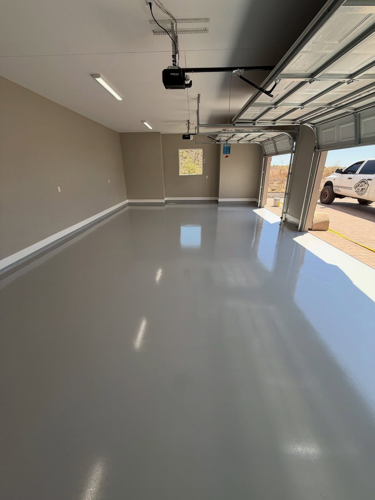 9 Garage Paint Colors for Doors, Floors, Walls and Ceiling 7 A spacious empty garage featuring glossy grey epoxy floors and neutral beige walls under bright lights.