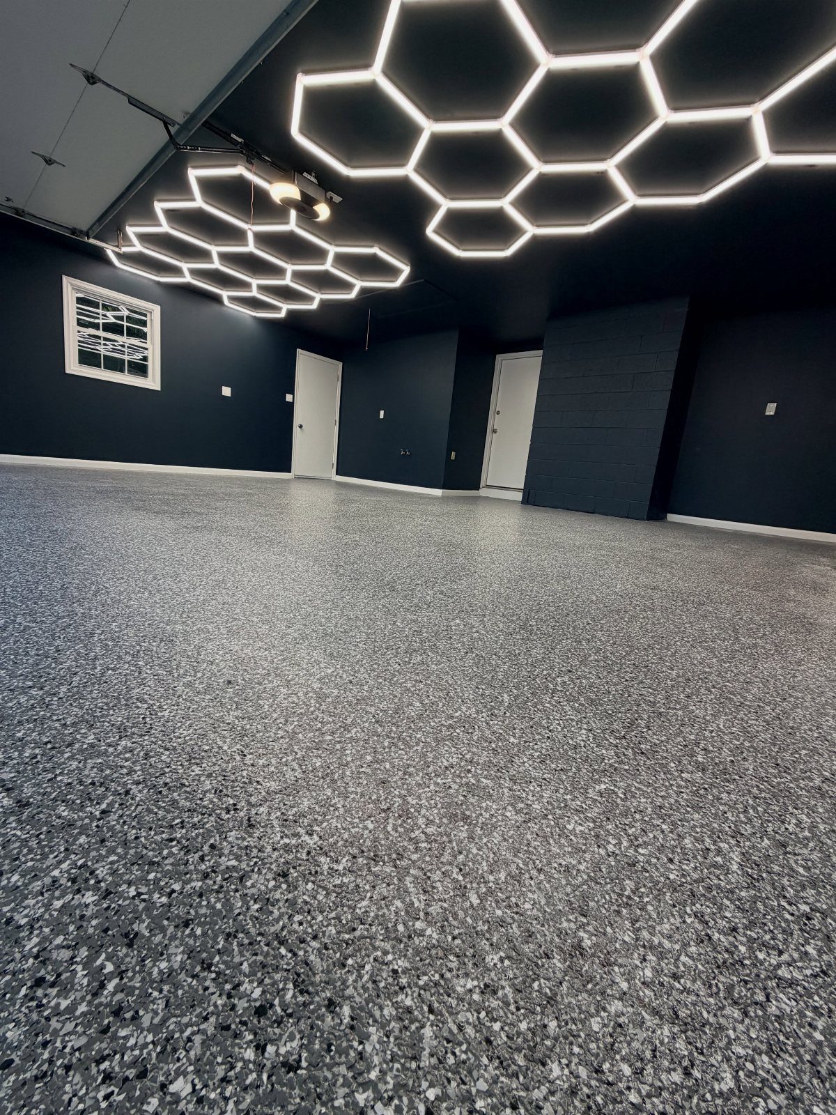 9 Garage Paint Colors for Doors, Floors, Walls and Ceiling 4 A dark garage with hexagonal LED lights on a black ceiling and speckled epoxy flooring.