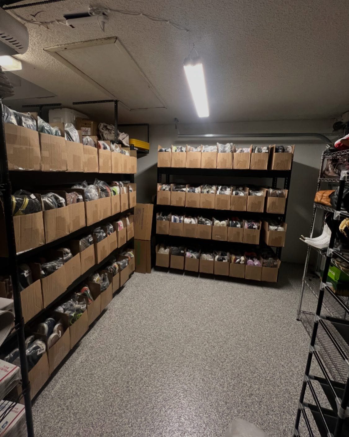 Black metal shelves filled with cardboard boxes containing organized shoe collections in a garage.
