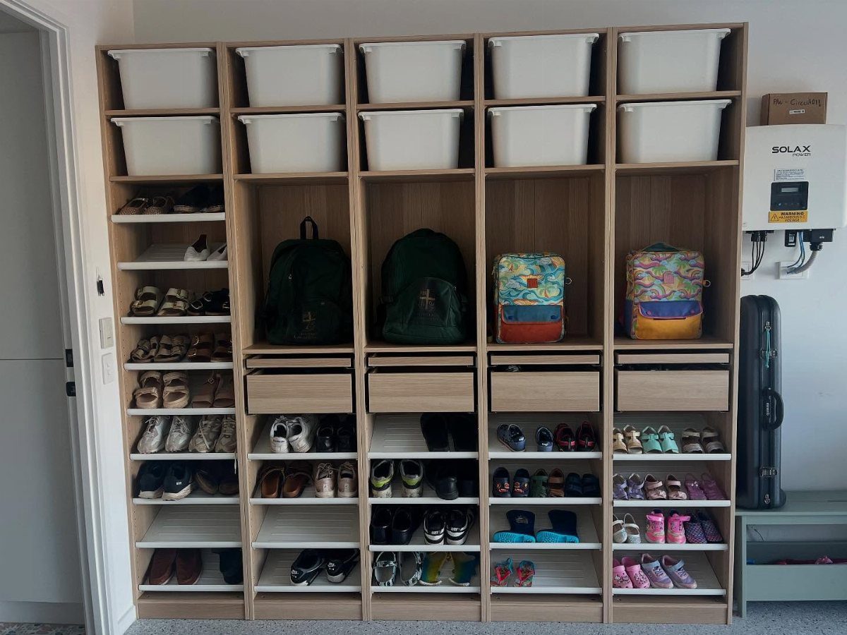Large wooden storage unit with compartments for bins, backpacks, and various shoes on shelves.