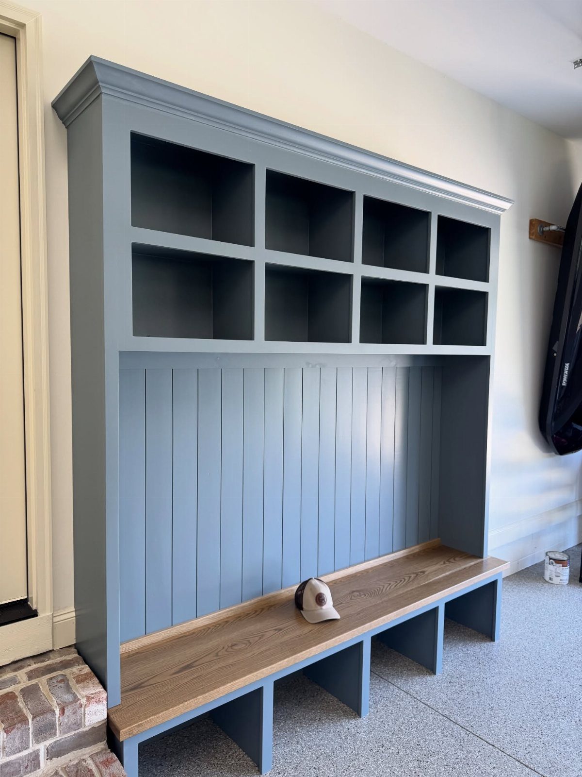 A blue built-in mudroom unit with upper cubbies and a long wooden bench seat.