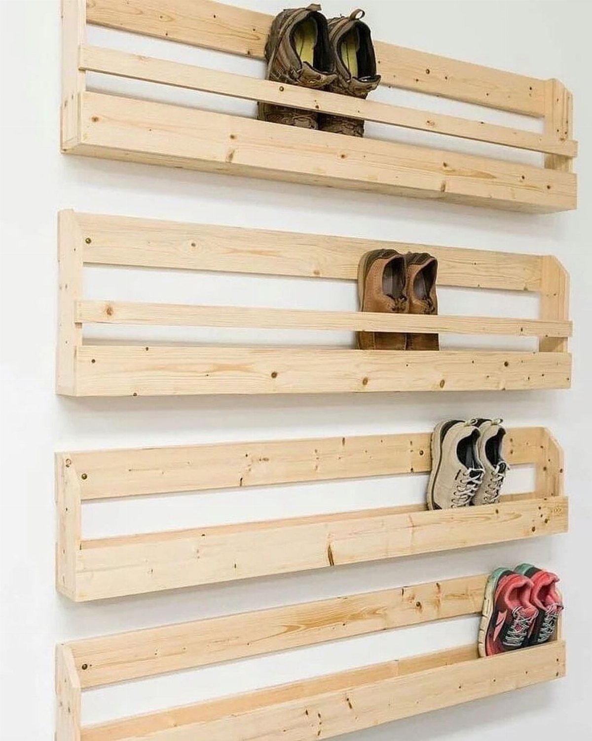 Four light wood wall-mounted shelves holding various pairs of shoes against a white wall.