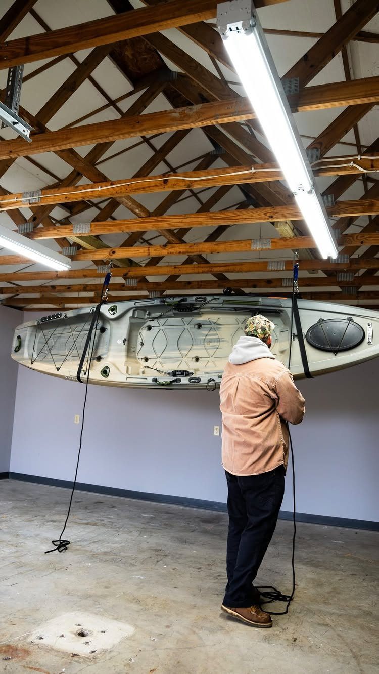 11 Garage Storage Inspiration and Ceiling Systems That Actually Fit 10 A man stands in a garage looking at a white kayak hanging from the ceiling rafters.