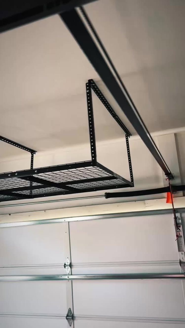 11 Garage Storage Inspiration and Ceiling Systems That Actually Fit 3 Black metal wire mesh storage rack mounted to a white garage ceiling above a door.