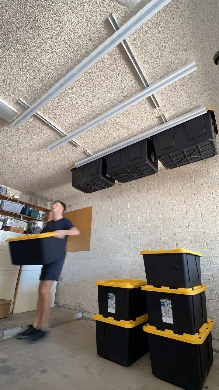 11 Garage Storage Inspiration and Ceiling Systems That Actually Fit 9 Black storage bins hanging from metal tracks mounted to a garage ceiling.