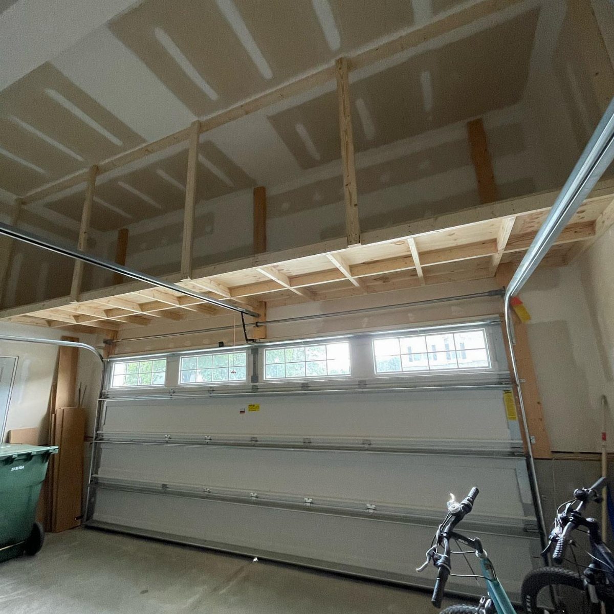 11 Garage Storage Inspiration and Ceiling Systems That Actually Fit 8 Wooden loft platform built into the garage ceiling above the garage door tracks.