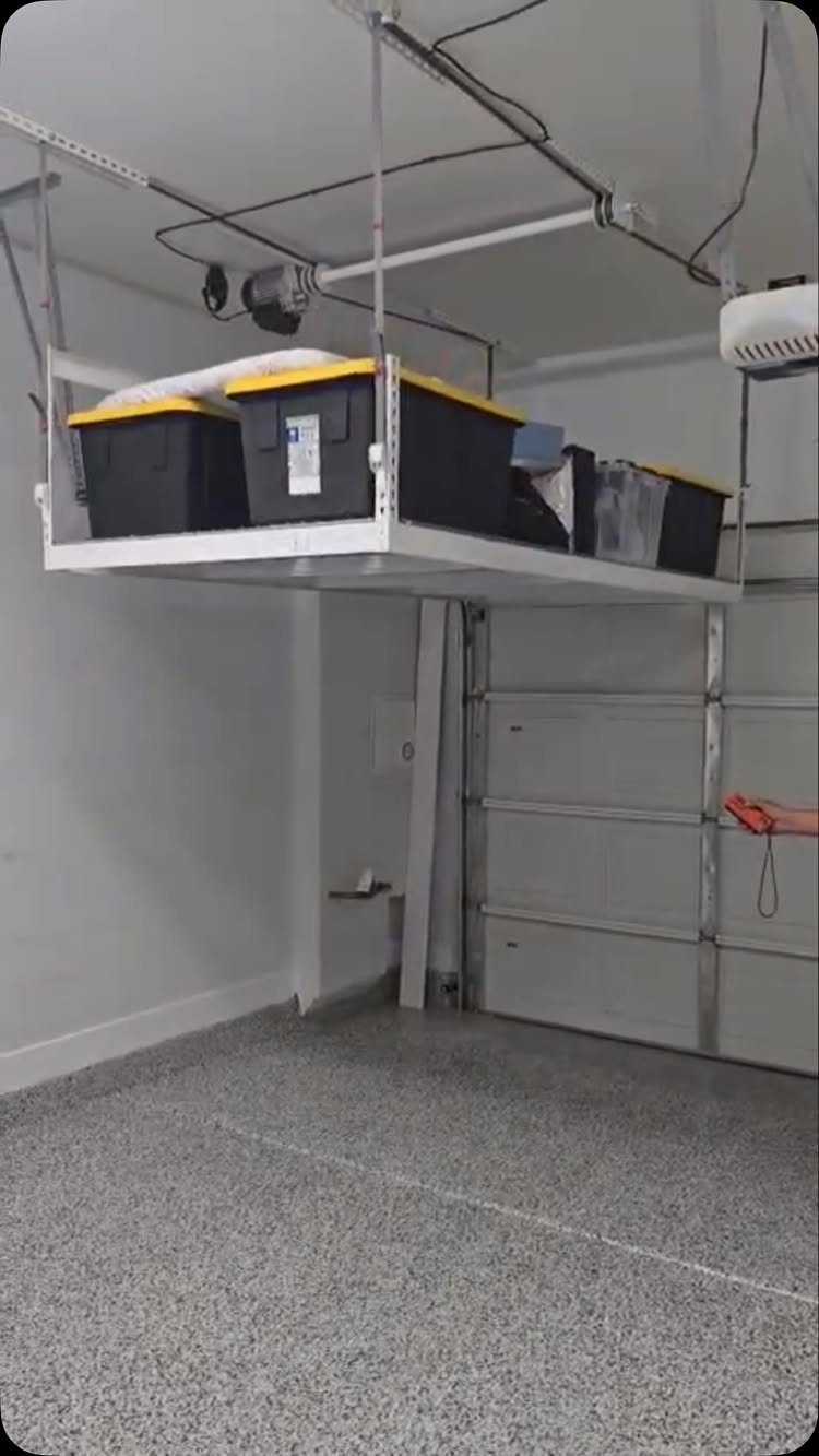 11 Garage Storage Inspiration and Ceiling Systems That Actually Fit 5 Motorized ceiling lift platform holding black and yellow storage bins in a clean garage.