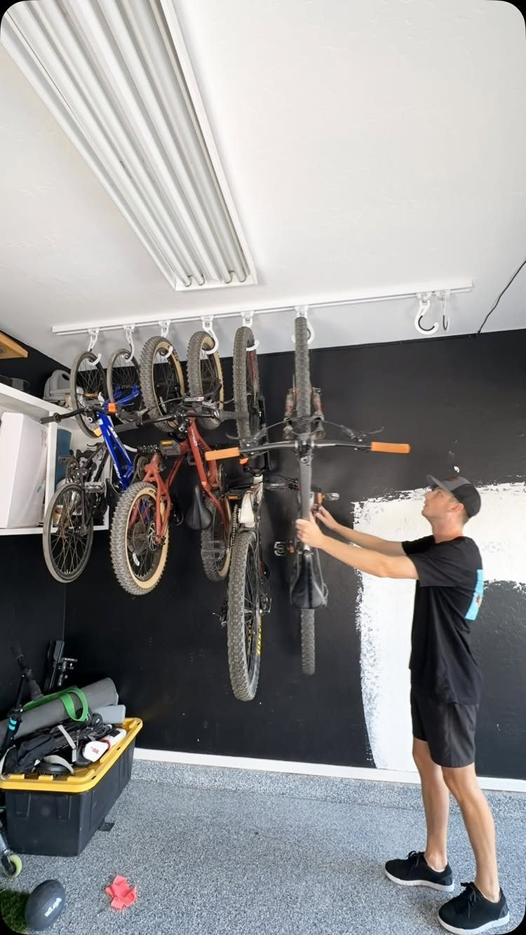 11 Garage Storage Inspiration and Ceiling Systems That Actually Fit 1 A man hanging a bicycle onto a multi-bike ceiling storage rack in a garage.