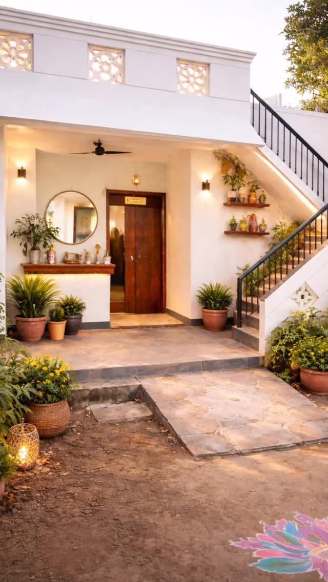 A covered porch area with white walls, wooden door, potted plants, and stone walkway.