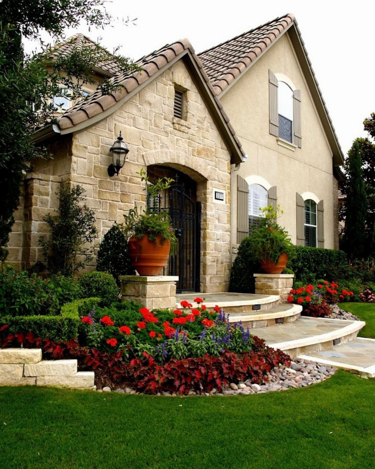 A stone house with vibrant red and blue flower beds in the front yard.