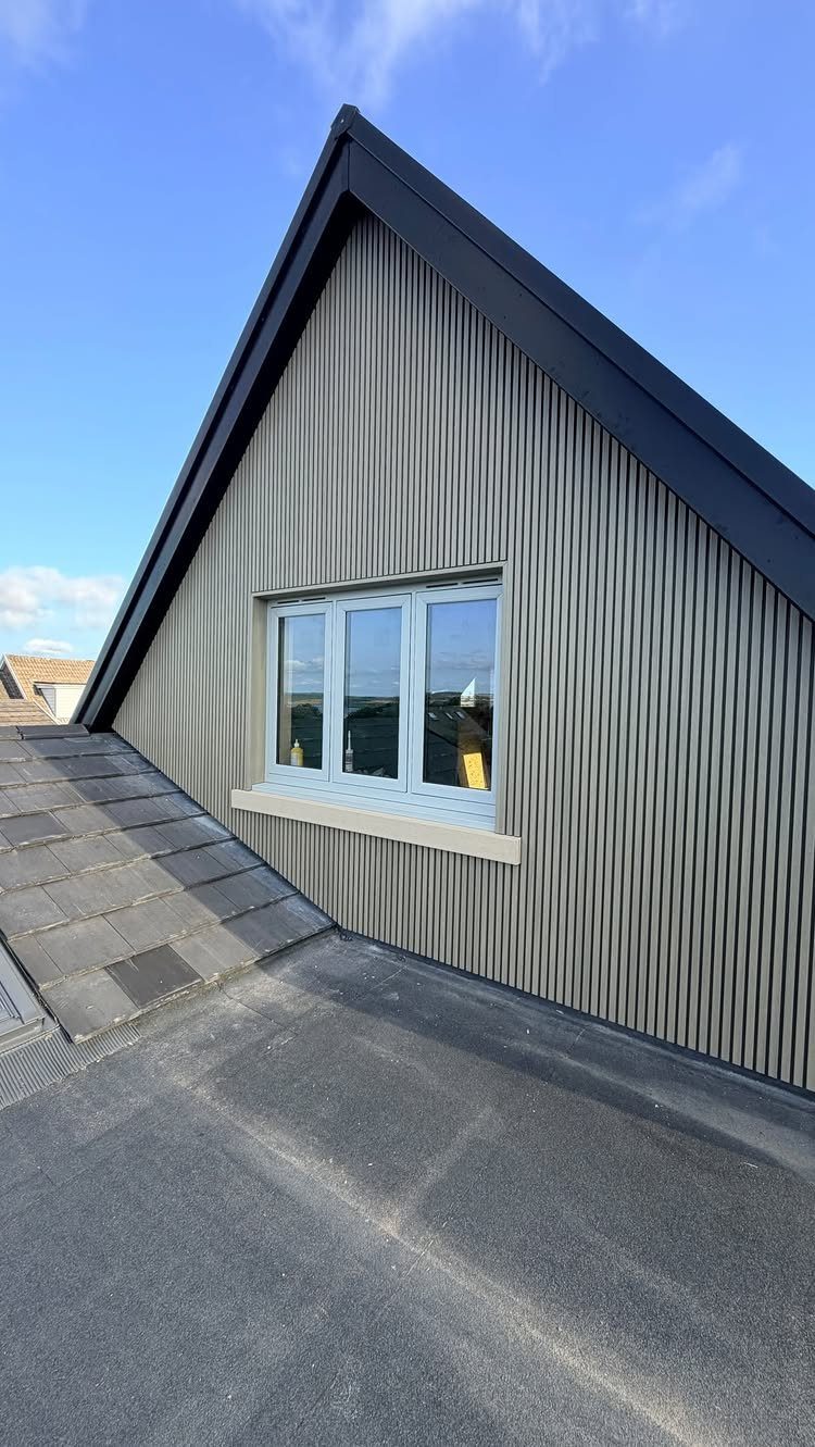 Grey vertical composite cladding on a house exterior with a white window and dark roof.