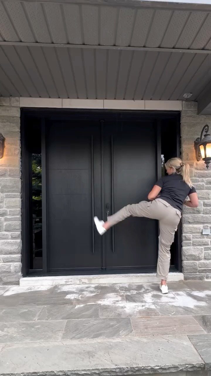 Woman posing playfully in front of a large, modern matte black double front door.