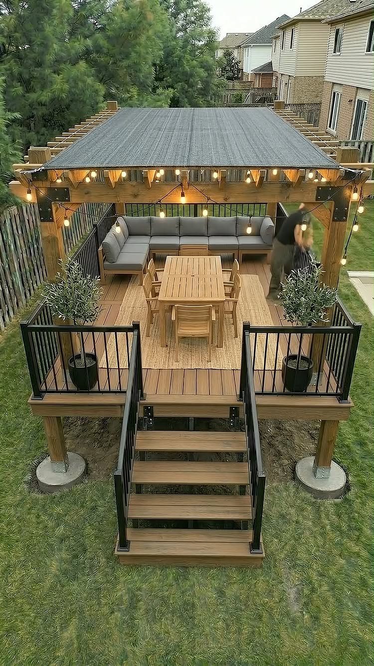 Wooden outdoor deck with a pergola, string lights, dining set, and grey sectional sofa.