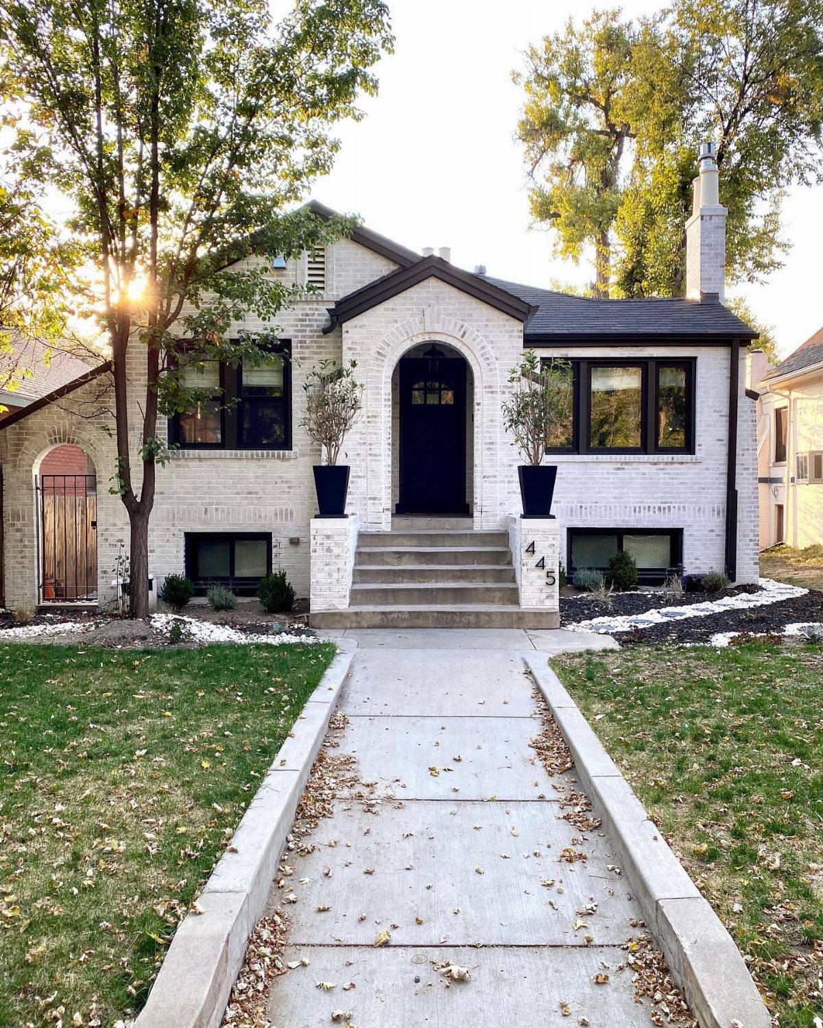 White painted brick house with a dark arched door and black window frames.
