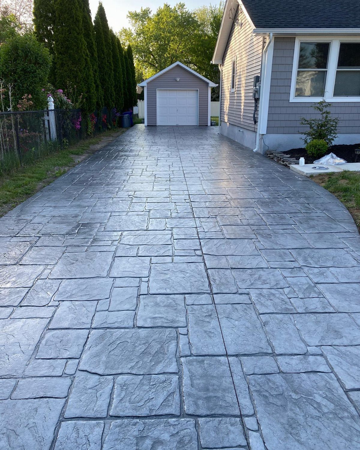 Grey stamped concrete driveway with a stone pattern leading toward a white garage and tan house.