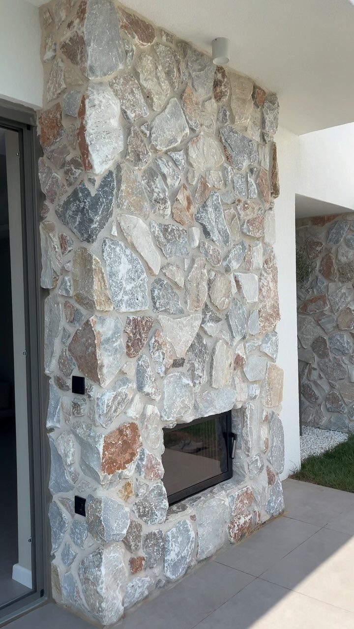 Natural multi-colored stone siding covering an outdoor wall with a built-in fireplace.