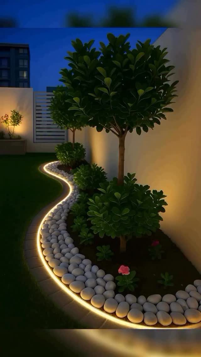 13 Landscaping Plans Layout Ideas to Draw From 11 A landscaped garden bed with a small tree, shrubs, and white stones outlined by glowing LED lights.