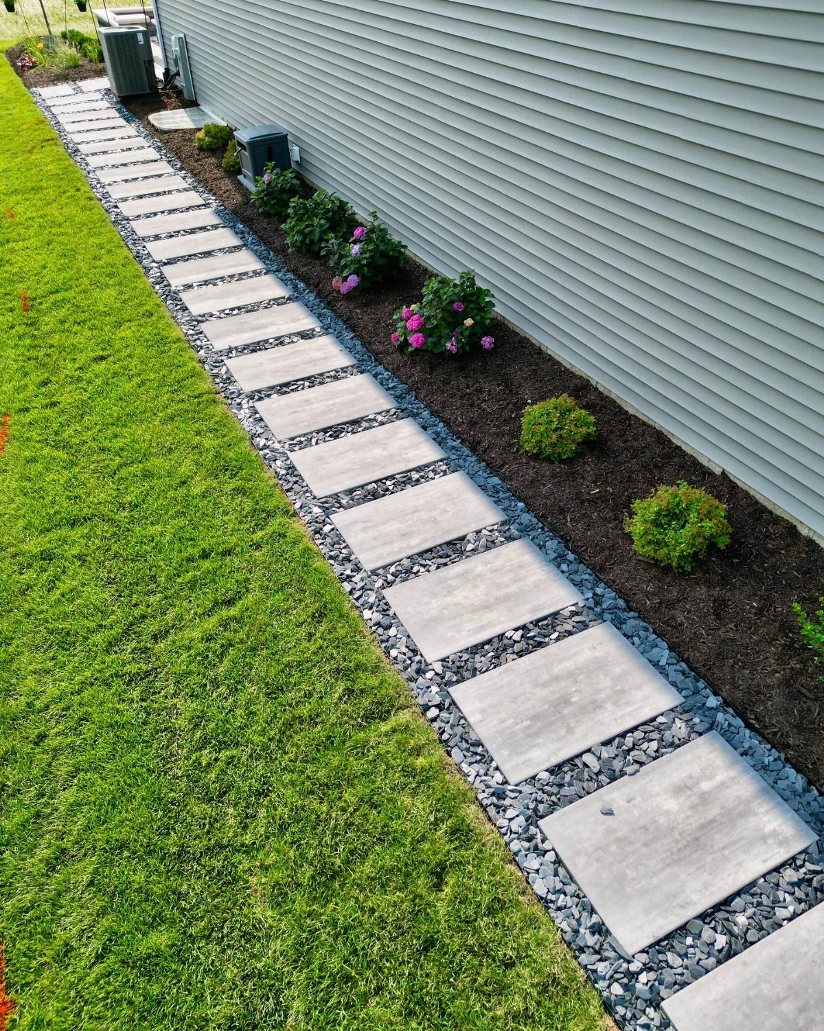 13 Landscaping Plans Layout Ideas to Draw From 12 Rectangular concrete pavers form a modern walkway through gravel next to a garden bed and house.