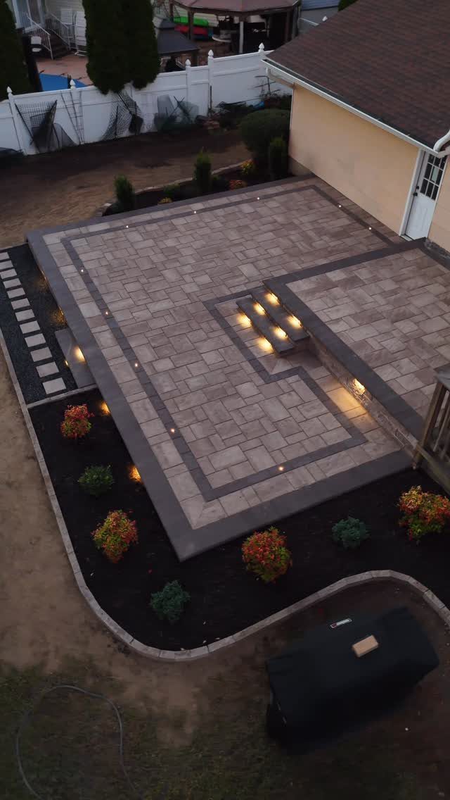 13 Landscaping Plans Layout Ideas to Draw From 2 Stone patio with geometric patterns, built-in lighting, and steps leading to a house.