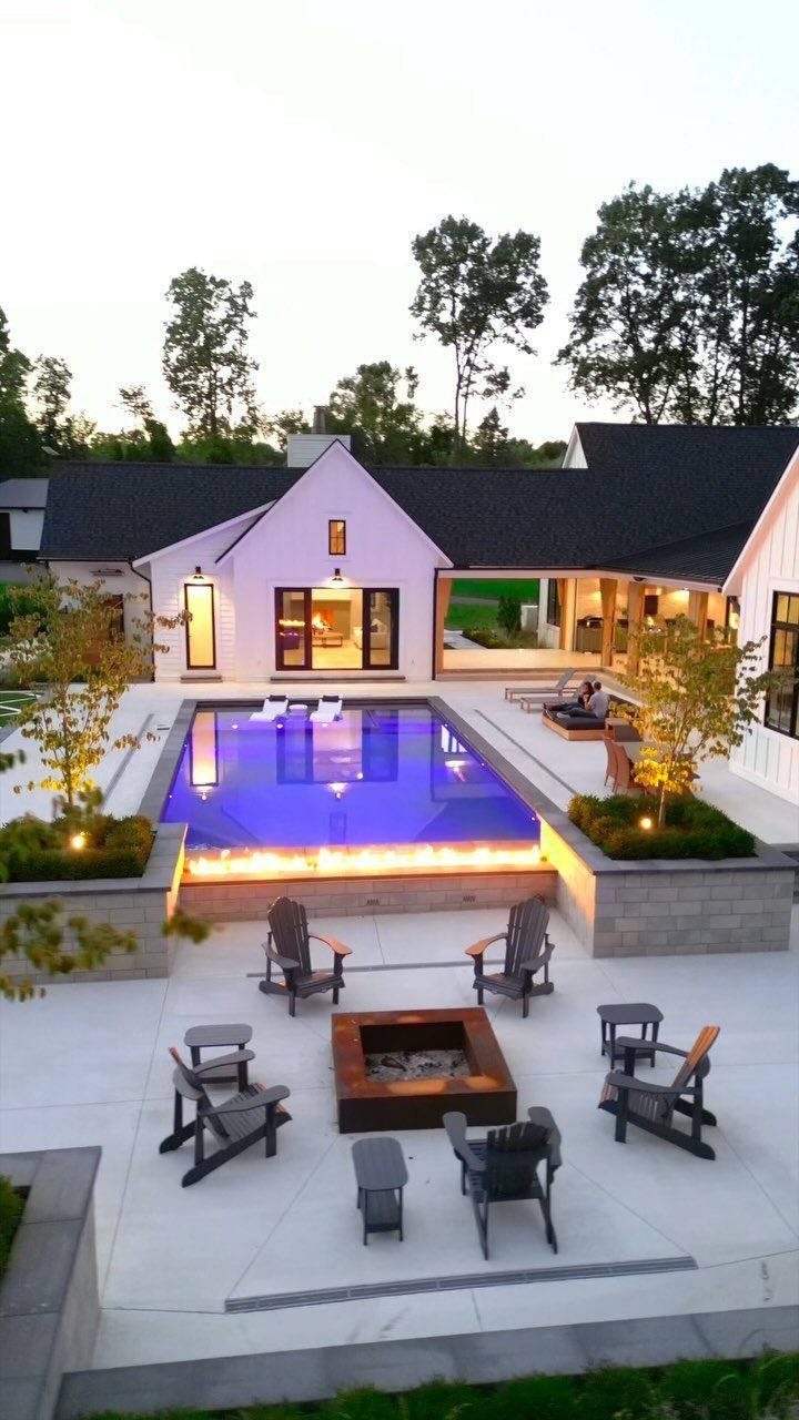 18 Large Yard Ideas for Patios, Pools, Outdoor Kitchens & More 15 A modern backyard with a glowing blue swimming pool, stone patio, and fire pit area.