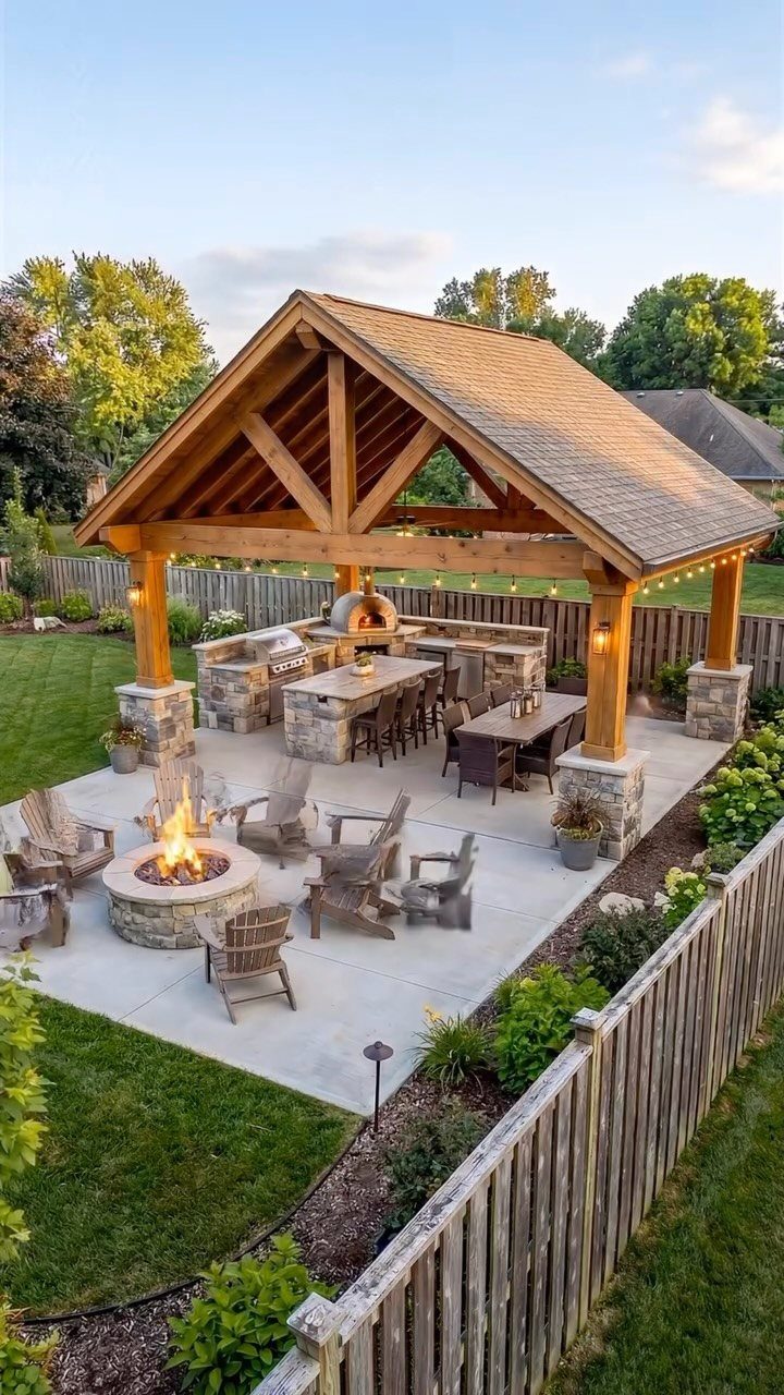 18 Large Yard Ideas for Patios, Pools, Outdoor Kitchens & More 16 Outdoor patio with a wooden pavilion, stone kitchen, dining area, and a fire pit with chairs.
