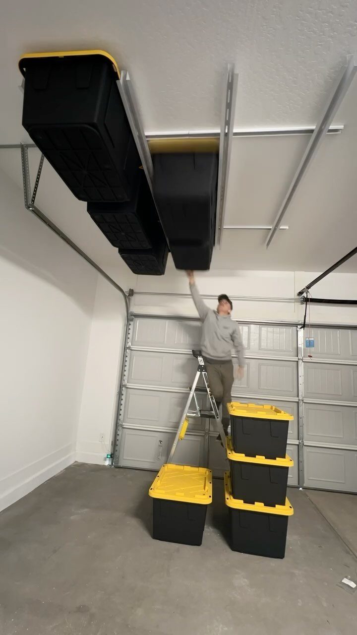 12 One Car Garage Workshop Layout Ideas That Save Space 12 A man on a ladder reaches for black storage bins hanging from a ceiling track system.