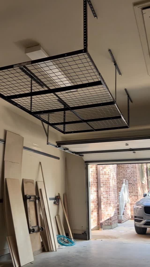 12 One Car Garage Workshop Layout Ideas That Save Space 10 Black metal wire mesh storage rack hanging from a garage ceiling above a workspace.