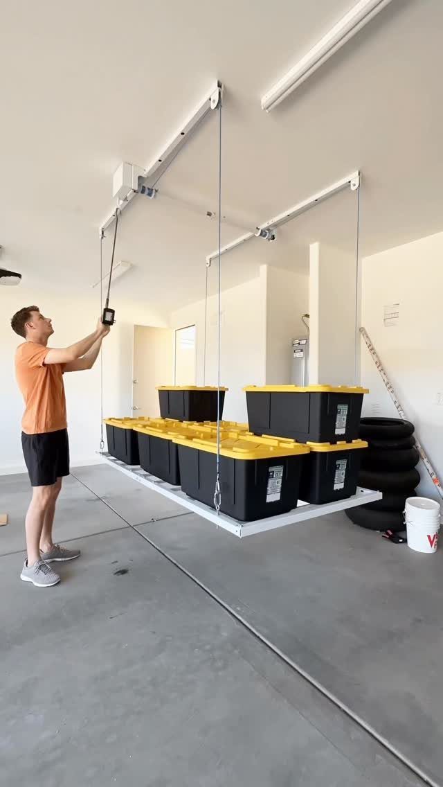 12 One Car Garage Workshop Layout Ideas That Save Space 8 A man operates a ceiling-mounted storage lift holding several black and yellow plastic bins in a garage.