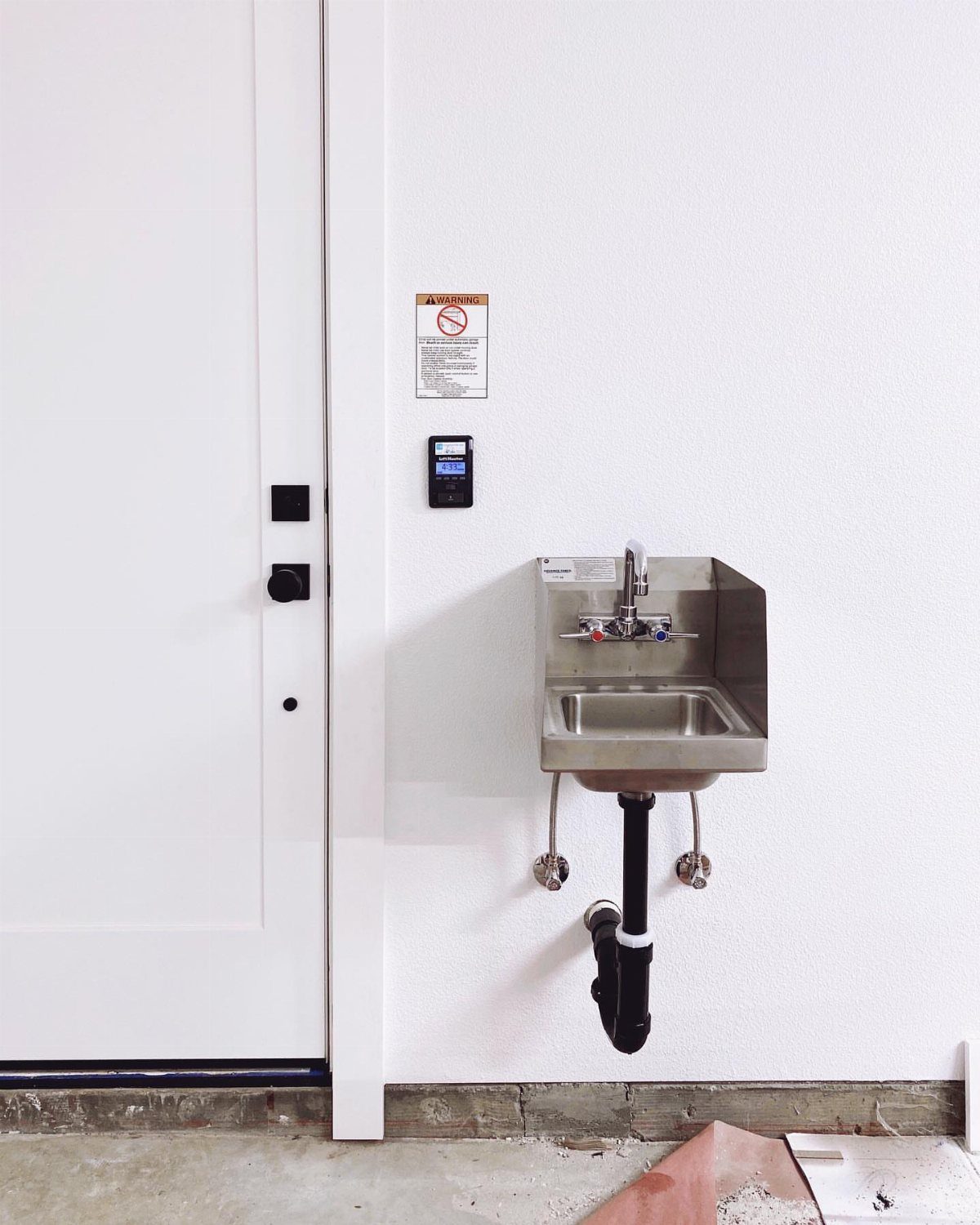 12 One Car Garage Workshop Layout Ideas That Save Space 2 Stainless steel utility sink mounted on a white wall with exposed plumbing underneath.
