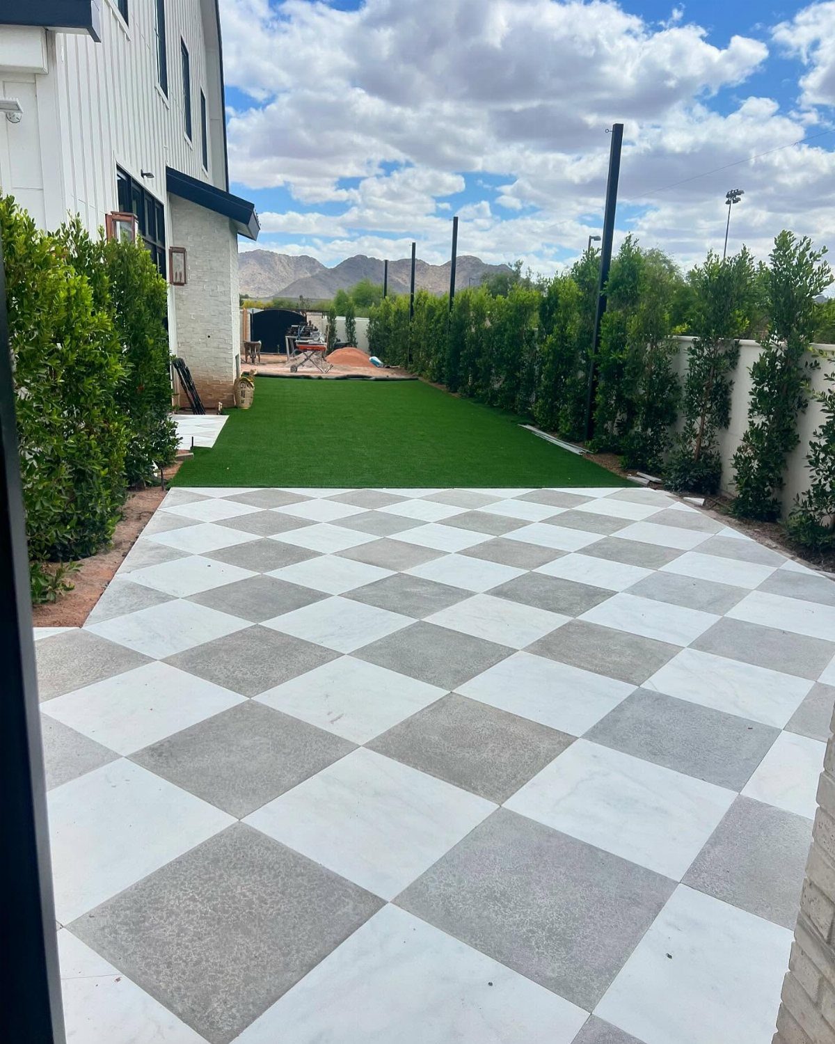 12 Paver Patio Ideas for Fire Pits, Poolside Lounges & Outdoor Rooms 5 Checkerboard pattern concrete pavers in white and grey arranged in a large outdoor patio area.