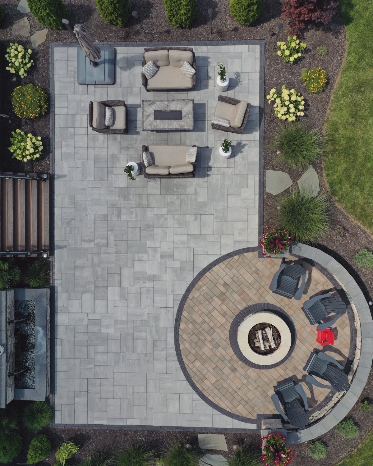 12 Paver Patio Ideas for Fire Pits, Poolside Lounges & Outdoor Rooms 3 Aerial view of a grey stone paver patio with outdoor furniture and a circular fire pit area.