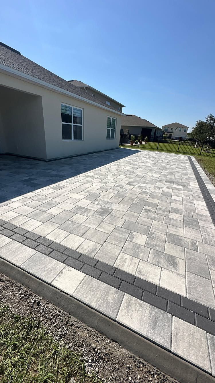 12 Paver Patio Ideas for Fire Pits, Poolside Lounges & Outdoor Rooms 11 Light grey and charcoal rectangular stone pavers installed in a large patio area next to a house.