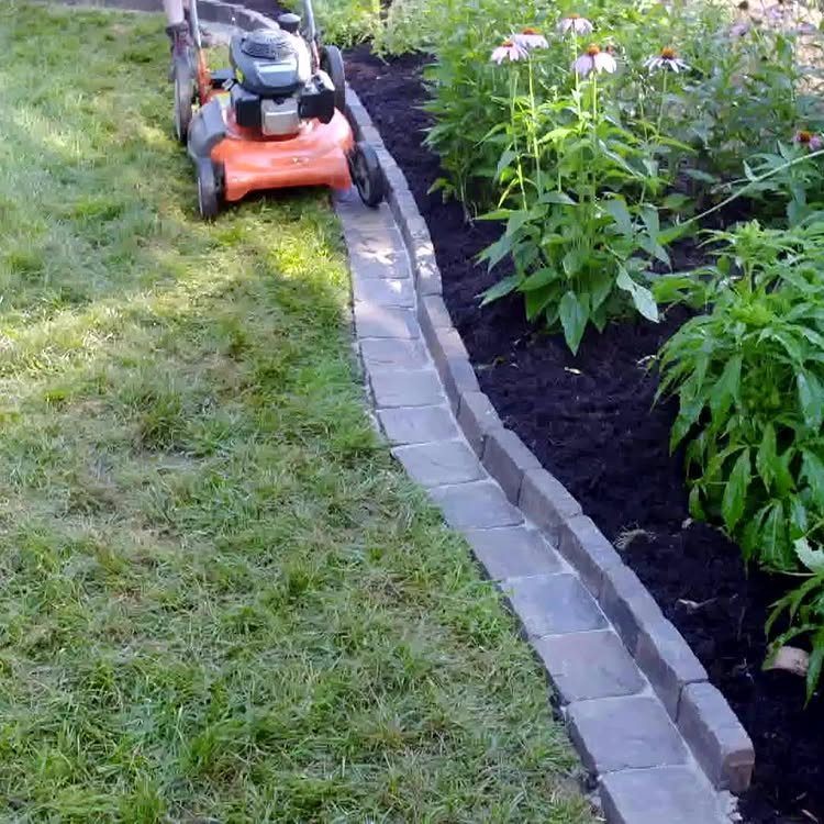 12 Paver Patio Ideas for Fire Pits, Poolside Lounges & Outdoor Rooms 4 Grey stone pavers create a curved border between a green lawn and a dark mulch garden bed.