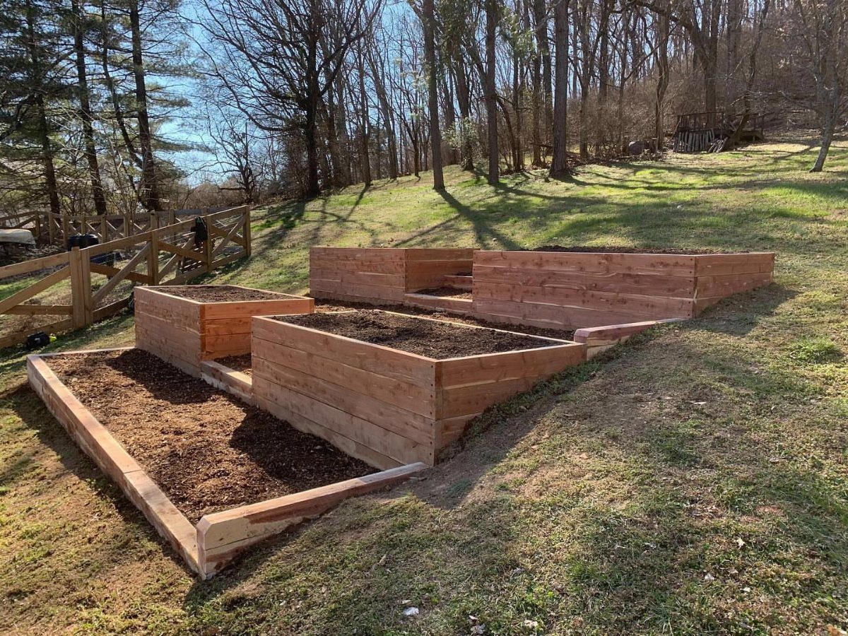 14 Raised Garden Bed Ideas for Every Yard and Budget 1 Wooden raised garden beds filled with dark soil on a grassy lawn near trees.
