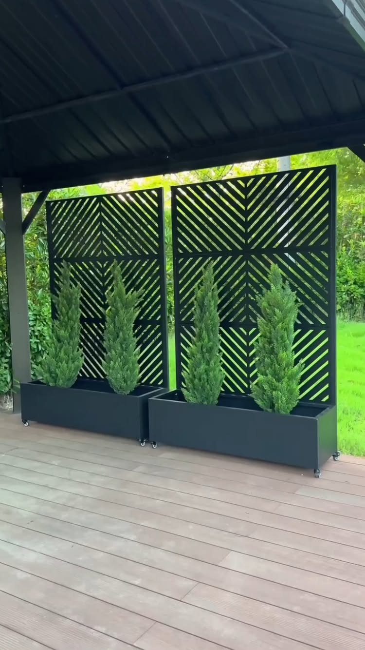 14 Raised Garden Bed Ideas for Every Yard and Budget 2 Two black planter boxes with tall green shrubs and geometric lattice trellises on a deck.