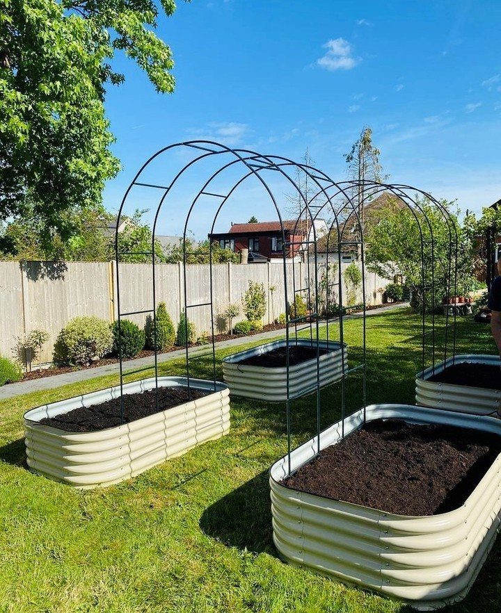 Corrugated metal raised garden beds with arched black metal trellises arranged on a green lawn.