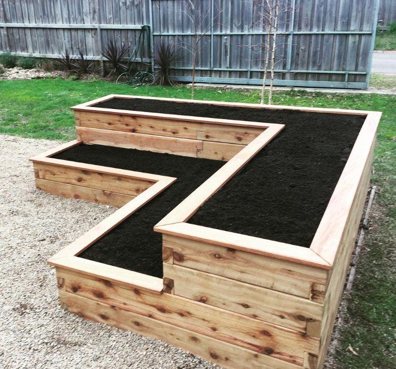 A multi-level wooden tiered raised garden bed filled with dark soil in a backyard.