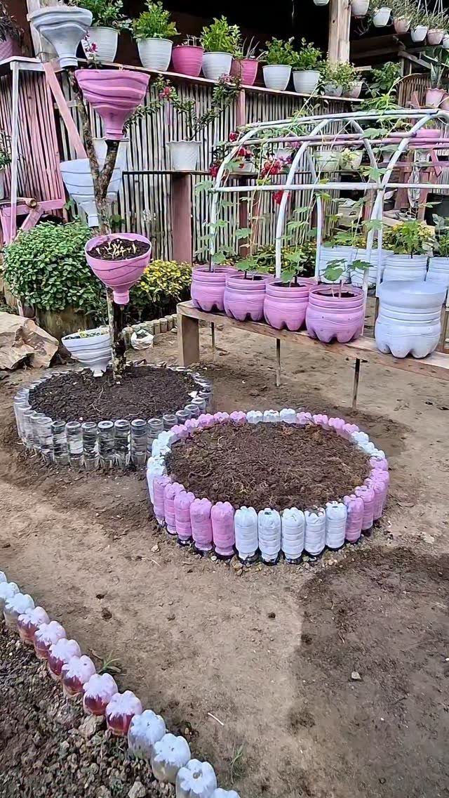 Circular raised garden beds constructed from pink and white plastic bottles filled with dark soil.