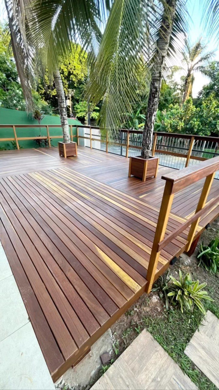 19 Small Backyard Wooden Deck Ideas 17 Wooden deck with brown planks built around two palm trees in a tropical garden.